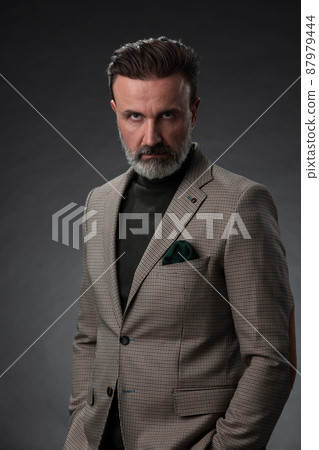 Portrait of a stylish elegant senior businessman with a beard and casual business clothes in photo studio isolated on dark background gesturing with hands 87979444