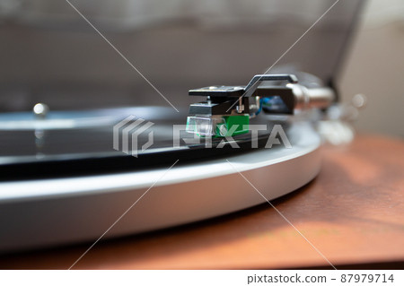 A close-up photo of a record needle tracing a groove on a vinyl record taken diagonally from the front. 87979714