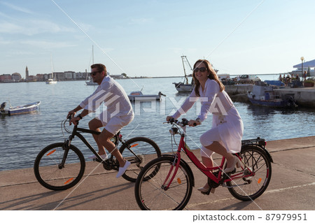Senior couple enjoying a beautiful morning together riding a bike by the sea. Selective focus Senior couple enjoying a beautiful morning together riding a bike by the sea. Selective focus 87979951