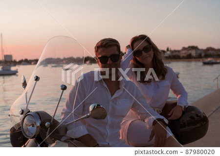 The couple enjoys a vacation while sitting on a scooter by the sea and enjoying the beautiful sunrise. Selective focus The couple enjoys a vacation while sitting on a scooter by the sea and enjoying the beautiful sunrise. Selective focus 87980020