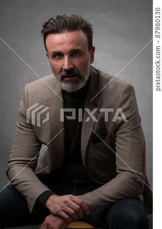 Portrait of a stylish elegant senior businessman with a beard and casual business clothes in photo studio isolated on dark background gesturing with hands Portrait of a stylish elegant senior businessman with a beard and casual business clothes in photo studio isolated on dark background gesturing with hands 87980130