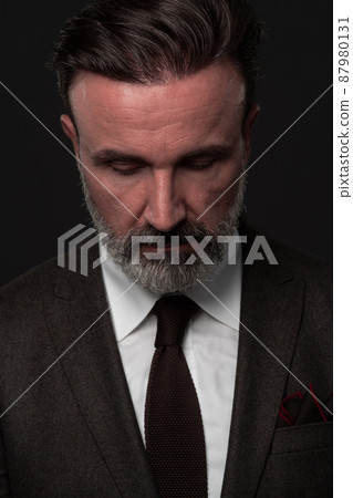 Portrait of a stylish elegant senior businessman with a beard and casual business clothes in photo studio isolated on dark background gesturing with hands Portrait of a stylish elegant senior businessman with a beard and casual business clothes in photo studio isolated on dark background gesturing with hands 87980131