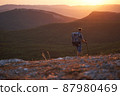 Young hiker with backpack and trekking poles walking along a mountain path at sunset with a smile. High quality photo. 87980469