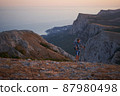 Young hiker with backpack and trekking crimea poles enjoying the scenery at sunset with a smile. High quality photo. 87980498