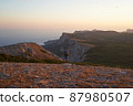 Young hiker with backpack and trekking poles enjoying the scenery at sunset with a smile. High quality photo. 87980507