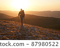 Young hiker with backpack and trekking crimea poles walking along a mountain path at sunset with a smile. High quality photo. 87980522