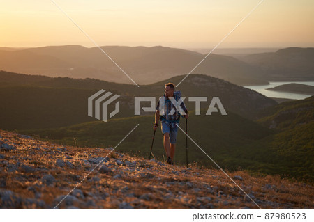 Hike mountain man hiking travel with backpack and trekking poles walking at adventure and sunset with a smile. High quality photo. 87980523