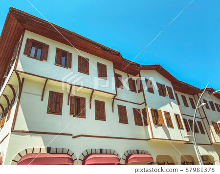 white residential building with many windows and a brown roof. house for the life of families in a hot country without heating. from below the house small shops with a red roof 87981378