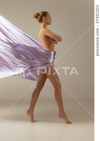 Full-length portrait of young beautiful woman covered with light purple silk fabrik isolated over beige studio background 87981855