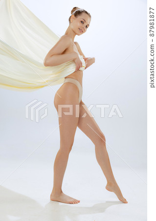 Full-length portrait of young beautiful woman in underwear covered with silk fabrik, posing isolated over gray studio background 87981877