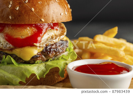 Tasty homemade burger with beef, tomatoes, onions, cheese and salad on a black stone background with copy space. Side view. fast food. Closeup. focus on cutlet. Tasty homemade burger with beef, tomatoes, onions, cheese and salad on a black stone background with copy space. Side view. fast food. Closeup. focus on cutlet. 87983439