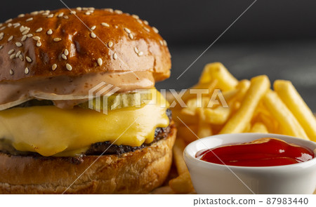 Tasty homemade burger with beef, tomatoes, onions, cheese and salad on a black stone background with copy space. Side view. fast food. Closeup. focus on cutlet. Tasty homemade burger with beef, tomatoes, onions, cheese and salad on a black stone background with copy space. Side view. fast food. Closeup. focus on cutlet. 87983440