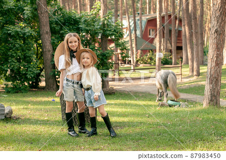 Friendly tween sisters hugging in courtyard of country house with pony in background Friendly tween sisters hugging in courtyard of country house with pony in background 87983450