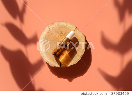 Amber glass dropper bottle on woodcut in the sunlight with eucalyptus flower shadows. Top view. Luxury and natural cosmetics presentation. Testers, beauty samples perfumery concept. Shades and lights 87983469