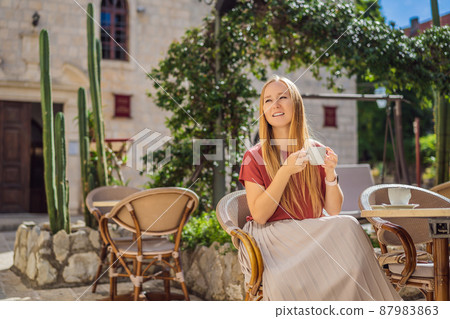 Young woman tourist drinks cofee in the old town of Budva. Travel to Montenegro concept Young woman tourist drinks cofee in the old town of Budva. Travel to Montenegro concept 87983863