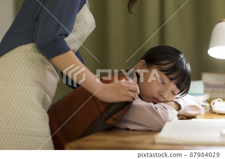 A mother who puts a blanket on her daughter who falls asleep at the desk A mother who puts a blanket on her daughter who falls asleep at the desk 87984029