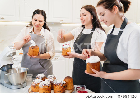a mother and daughters decorate icing, dried berries and flowers easter cakes. a mother and daughters decorate icing, dried berries and flowers easter cakes. 87984426