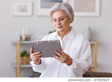 Focused mature woman using tablet at home Focused mature woman using tablet at home 87984929