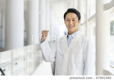 A man in his 30s wearing a white coat and smiling while looking at the camera, fist pump, medical worker/researcher, image 87991980