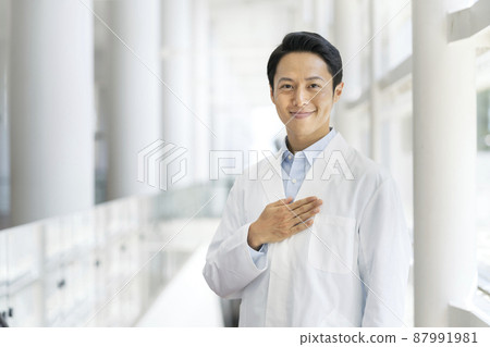 Image of a male medical worker / researcher in his thirties smiling looking at the camera in a white coat with his hands on his chest 87991981