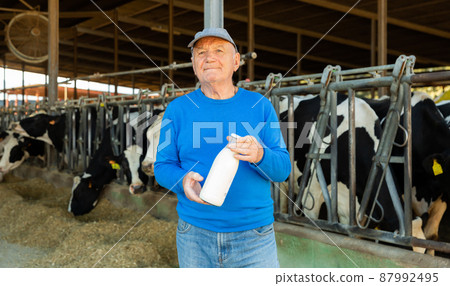 Farmer with bottle of milk in cowshed 87992495