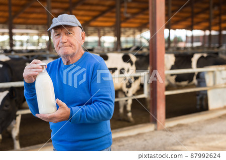 Farmer with bottle of milk in cowshed 87992624