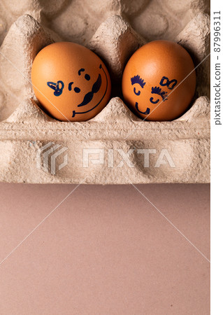 Close-up of creative female and male drawing on brown eggs in carton 87996311