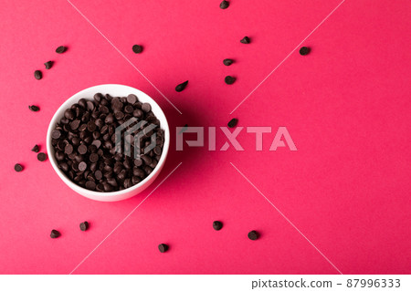 Directly above view of bowl with fresh chocolate chips scattered by copy space over pink background 87996333