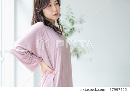 一名身體狀況不佳的婦女,穿著房間衣服時把手放在腰上 一名身體狀況不佳的婦女,穿著房間衣服時把手放在腰上 87997523