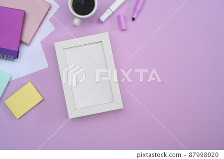 White empty picture frame, coffee cup and stationery on purple background. 87998020
