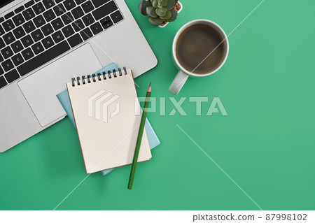 Stylish workplace with laptop computer, notepad and coffee cup on green background. 87998102
