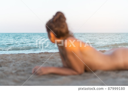 Naked woman lying on sandy beach and having sunbath Naked woman lying on sandy beach and having sunbath 87999180