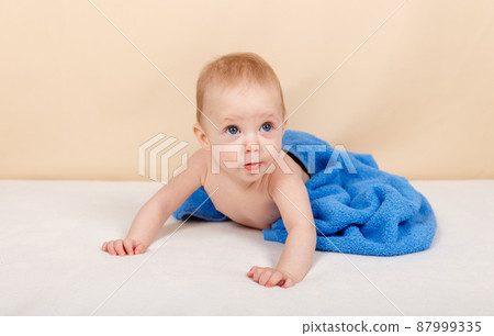 Baby boy wearing diaper and blue towel after bath or shower on the bed 87999335