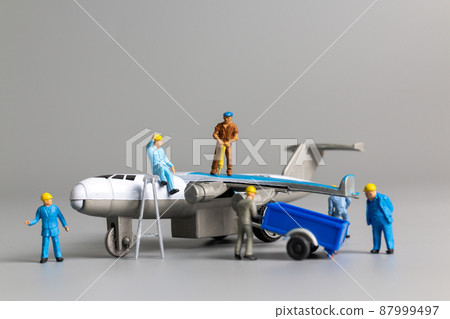 Miniature worker team checking and repairing airplane on gray background. Miniature worker team checking and repairing airplane on gray background. 87999497