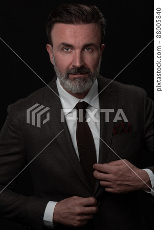 Portrait of a stylish elegant senior businessman with a beard and casual business clothes in photo studio adjusting suit 88005840