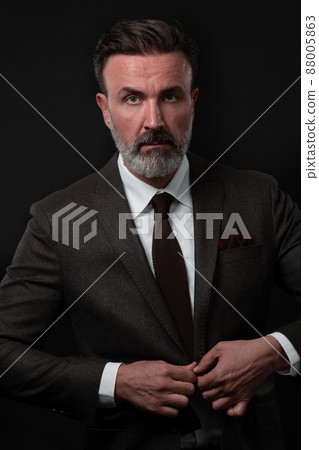 Portrait of a stylish elegant senior businessman with a beard and casual business clothes in photo studio adjusting suit 88005863