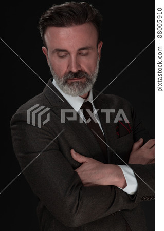 Portrait of a stylish elegant senior businessman with a beard and casual business clothes in photo studio isolated on dark background gesturing with hands 88005910
