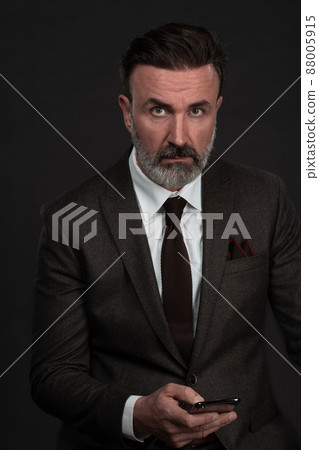 Portrait of adult businessman wearing trendy suit and sitting in modern studio on stylish chair against the black background Portrait of adult businessman wearing trendy suit and sitting in modern studio on stylish chair against the black background 88005915