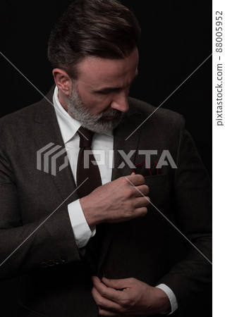 Portrait of a stylish elegant senior businessman with a beard and casual business clothes in photo studio adjusting suit Portrait of a stylish elegant senior businessman with a beard and casual business clothes in photo studio adjusting suit 88005952