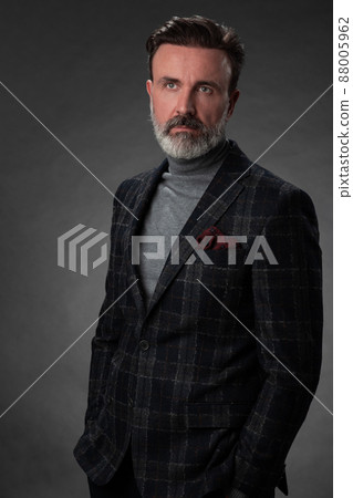 Portrait of a stylish elegant senior businessman with a beard and casual business clothes in photo studio isolated on dark background gesturing with hands 88005962