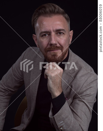 Portrait of adult businessman wearing trendy suit and sitting in modern studio on stylish chair against the black background 88006059