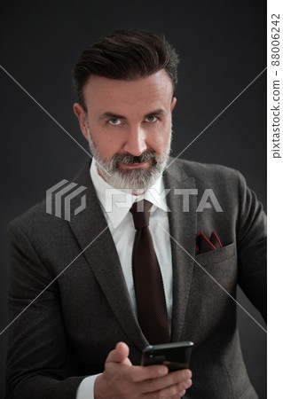Portrait of adult businessman wearing trendy suit and sitting in modern studio on stylish chair against the black background 88006242
