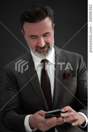 Portrait of adult businessman wearing trendy suit and sitting in modern studio on stylish chair against the black background 88006362