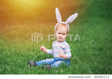 Toddler egg hunter close-up in grass with bunny ears... 88008112