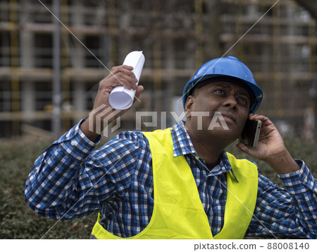 Indian or Somali engineer with safety jacket and helmet talking on mobile phone on construction site Indian or Somali engineer with safety jacket and helmet talking on mobile phone on construction site 88008140