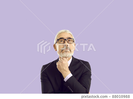 Pensive senior businessman in glasses looking up at copy space. Portrait of wise experienced mature man in suit and eyeglasses thinking about his business project, isolated on solid purple background Pensive senior businessman in glasses looking up at copy space. Portrait of wise experienced mature man in suit and eyeglasses thinking about his business project, isolated on solid purple background 88010988