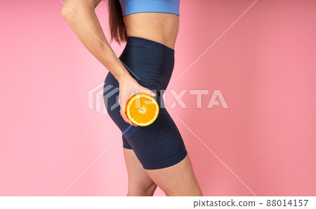 Woman in fashionable sportswear with orange fruit on pink background. Healthy lifestyle concept. Indoor studio shot, cellulite concept Woman in fashionable sportswear with orange fruit on pink background. Healthy lifestyle concept. Indoor studio shot, cellulite concept 88014157