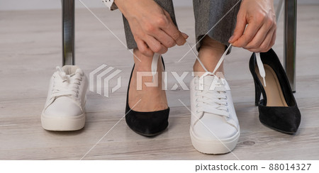 Close-up business woman takes off her shoes puts on white leather sneakers. Close-up business woman takes off her shoes puts on white leather sneakers. 88014327