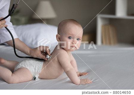 Serious baby patient examined by pediatrician on double bed at home 88014650