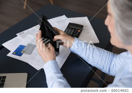 Senior woman sit at desk opening empty purse, above view Senior woman sit at desk opening empty purse, above view 88014681